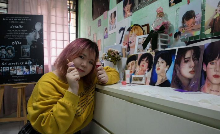 Ms Ng Kwok Ching poses with the BTS portraits she drew and her Loveholic Beauty cosmetics