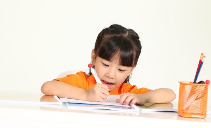 an asian child writing on a desk