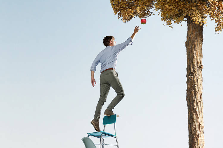 a man reaching for an apple on stacked chairs