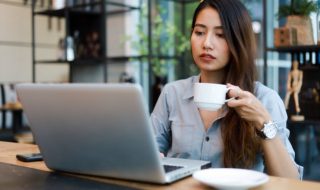 asian woman drinking coffee while working in a cafe