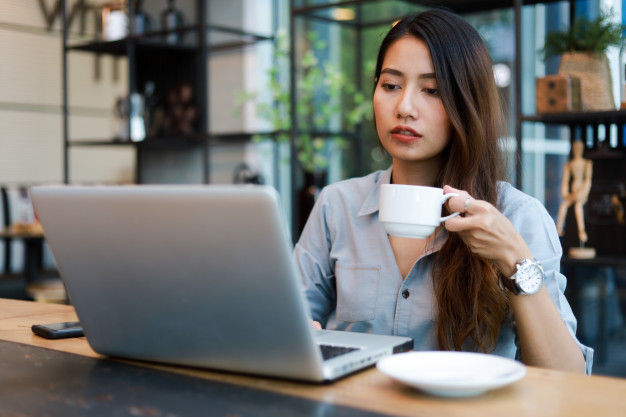 asian woman drinking coffee while working in a cafe