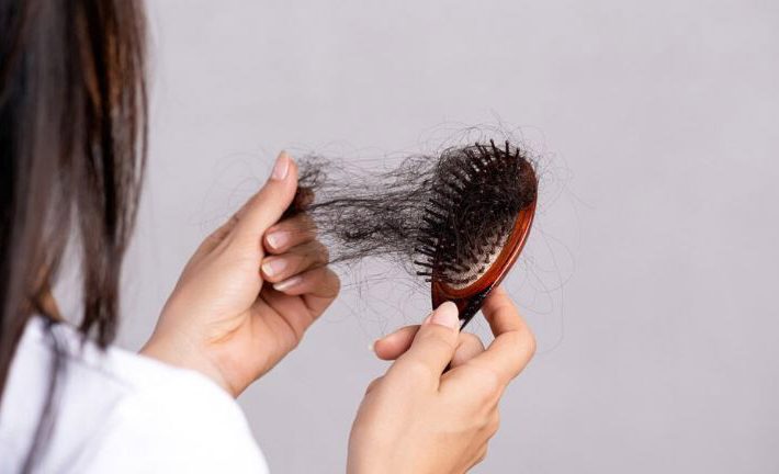 a woman looking at her hair loss on a comb