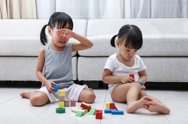 a young child crying in front of her sister