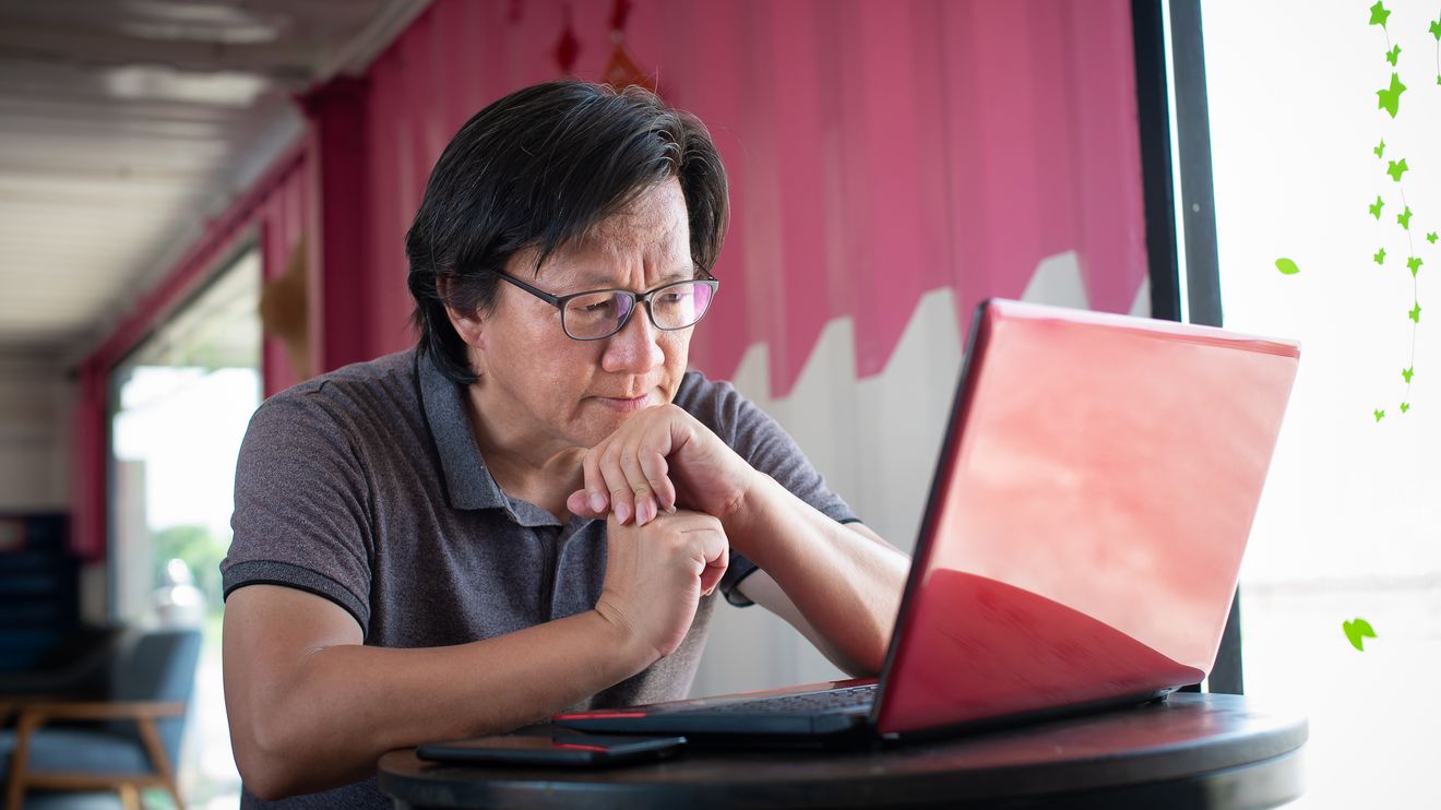 an asian man looking at his laptop