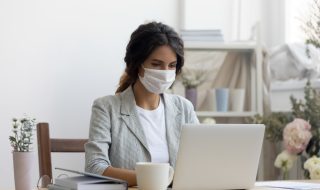 a woman with a face mask working on her laptop