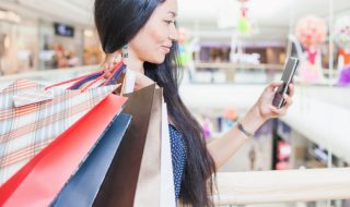 an asian woman carrying shopping bags and looking at her phone