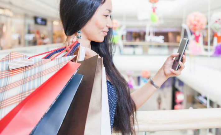 an asian woman carrying shopping bags and looking at her phone