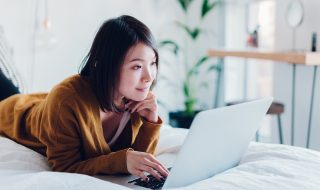 a female student woking on her laptop in bed