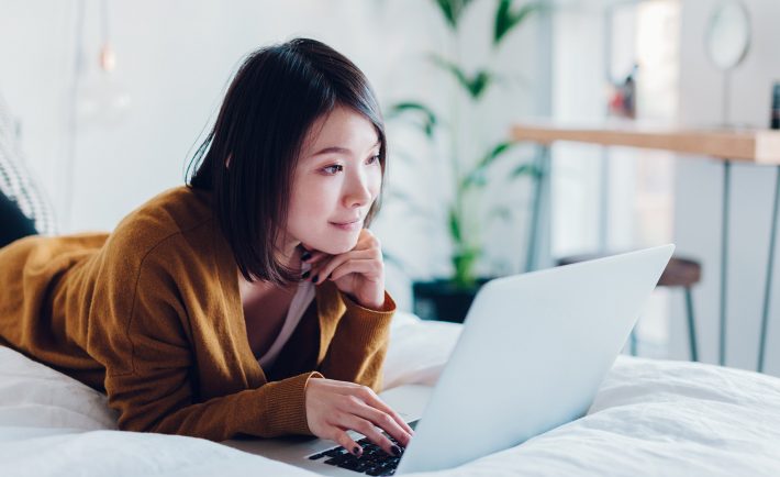 a female student woking on her laptop in bed