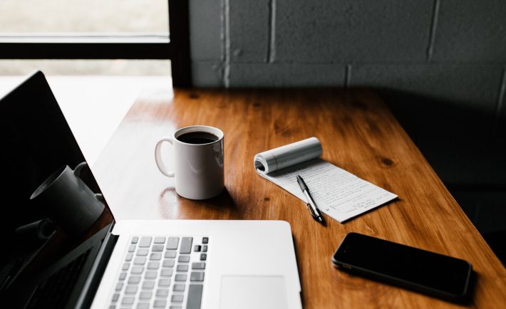 a laptop, coffee mug, and notepad on a desk