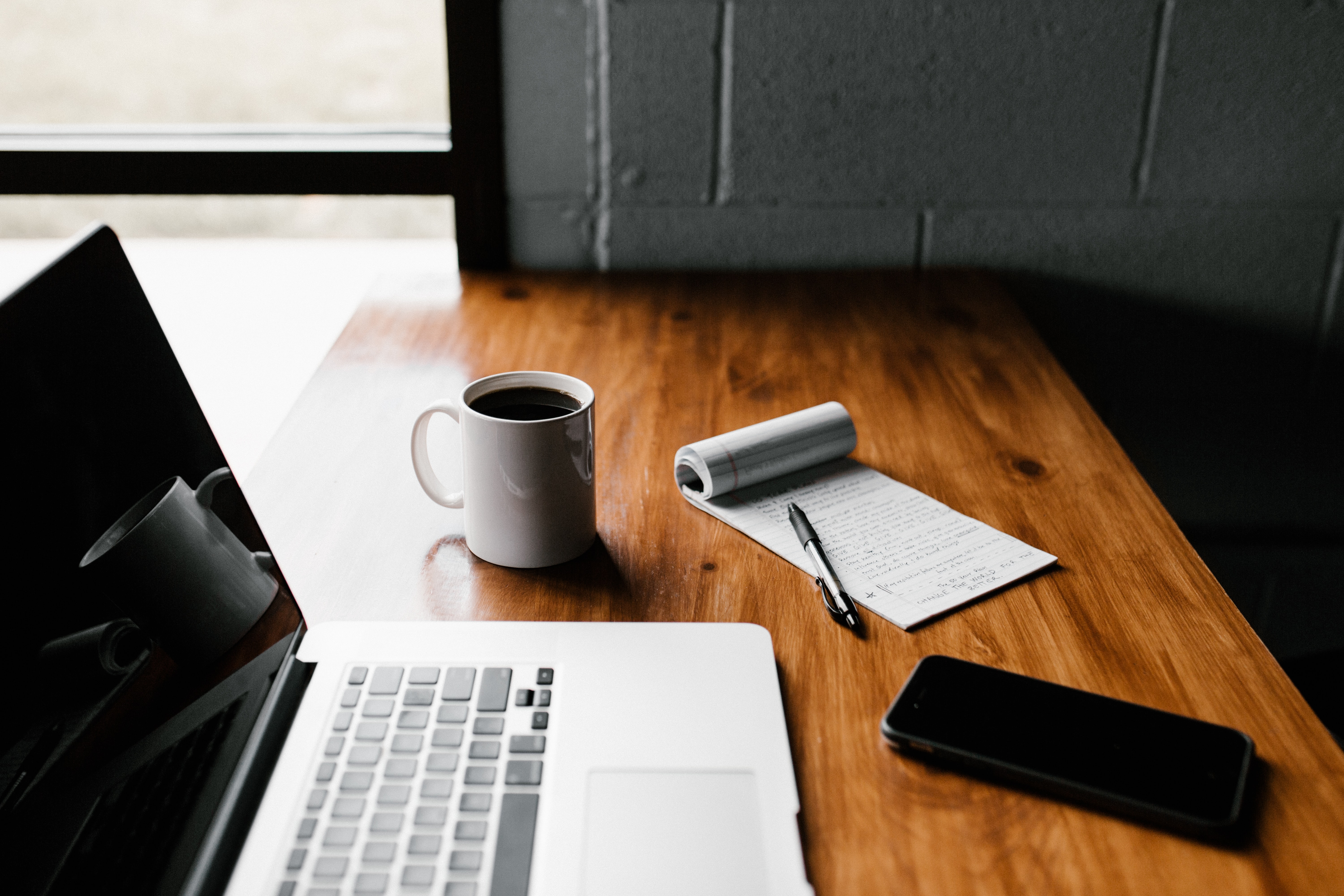 a laptop, coffee mug, and notepad on a desk