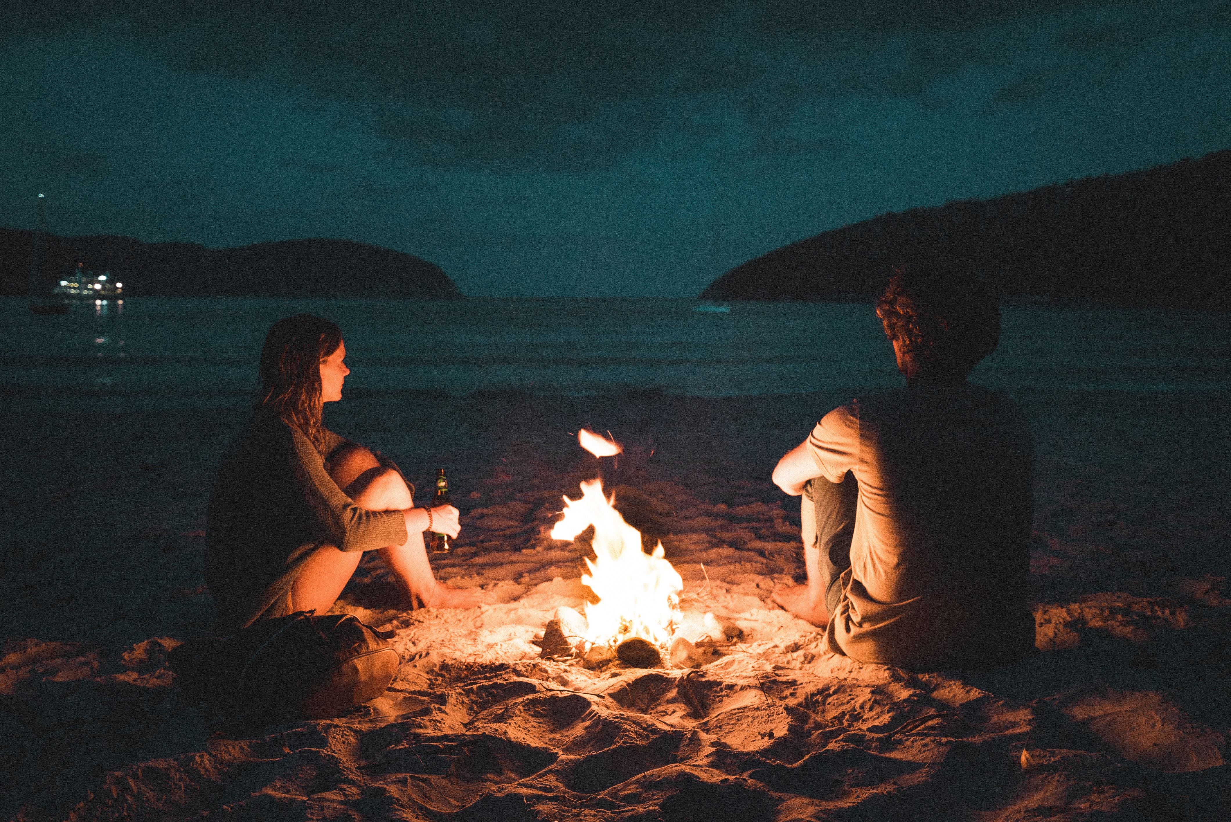 a couple chilling by the beach with a bonfire