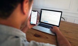 man looking at stocks using his phone and laptop