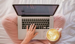 lady using a MacBook while holding a cup of latte