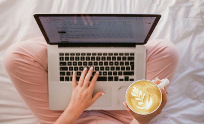 lady using a MacBook while holding a cup of latte