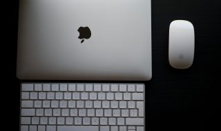 Apple laptop, keyboard & mouse on a black surface