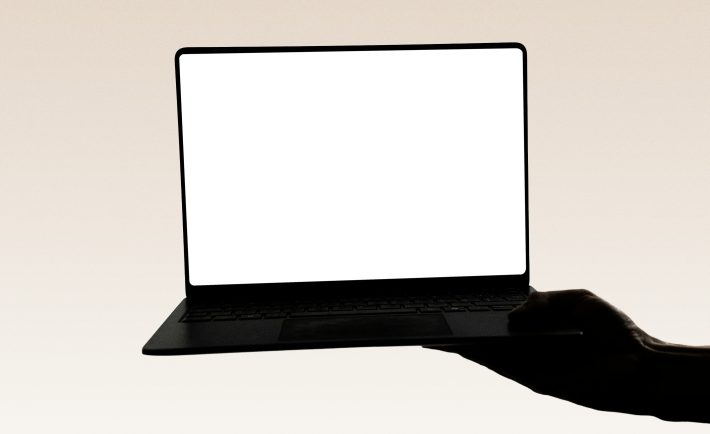 a hand holding a laptop with a white screen
