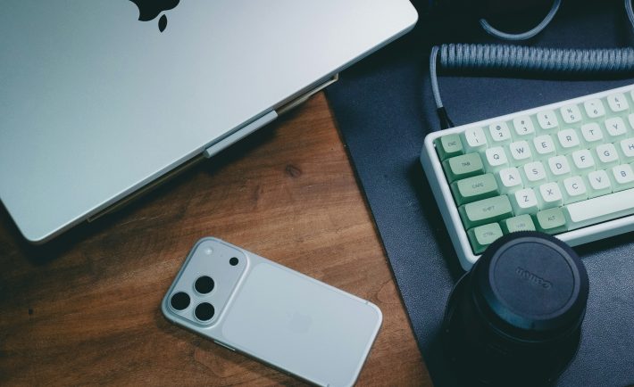a work desk with a laptop, smartphone, and keyboard