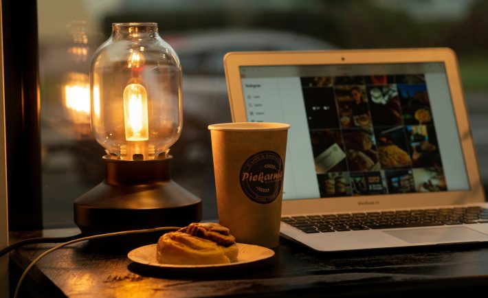 laptop, coffee, pastry, and a lamp on a desk